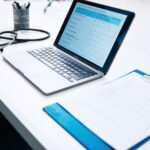 Laptop displaying claim assessment form with medical documents and stethoscope on desk